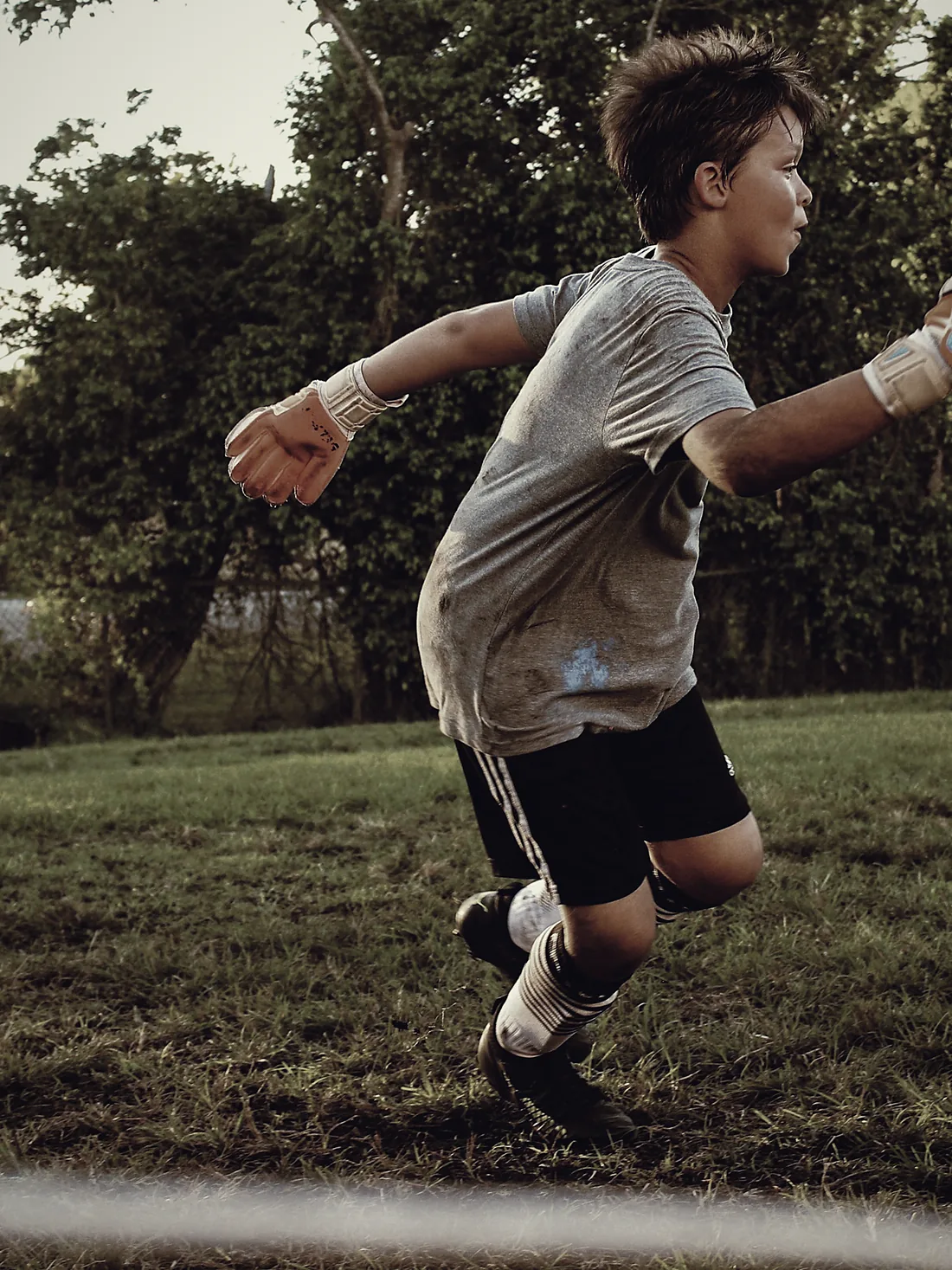 Portero infantil corriendo con el balón en las manos, a luz dorada