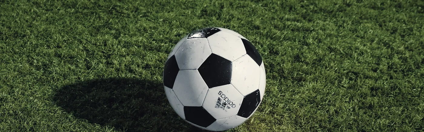 Balón de fútbol sobre el césped, con su sombra alargada