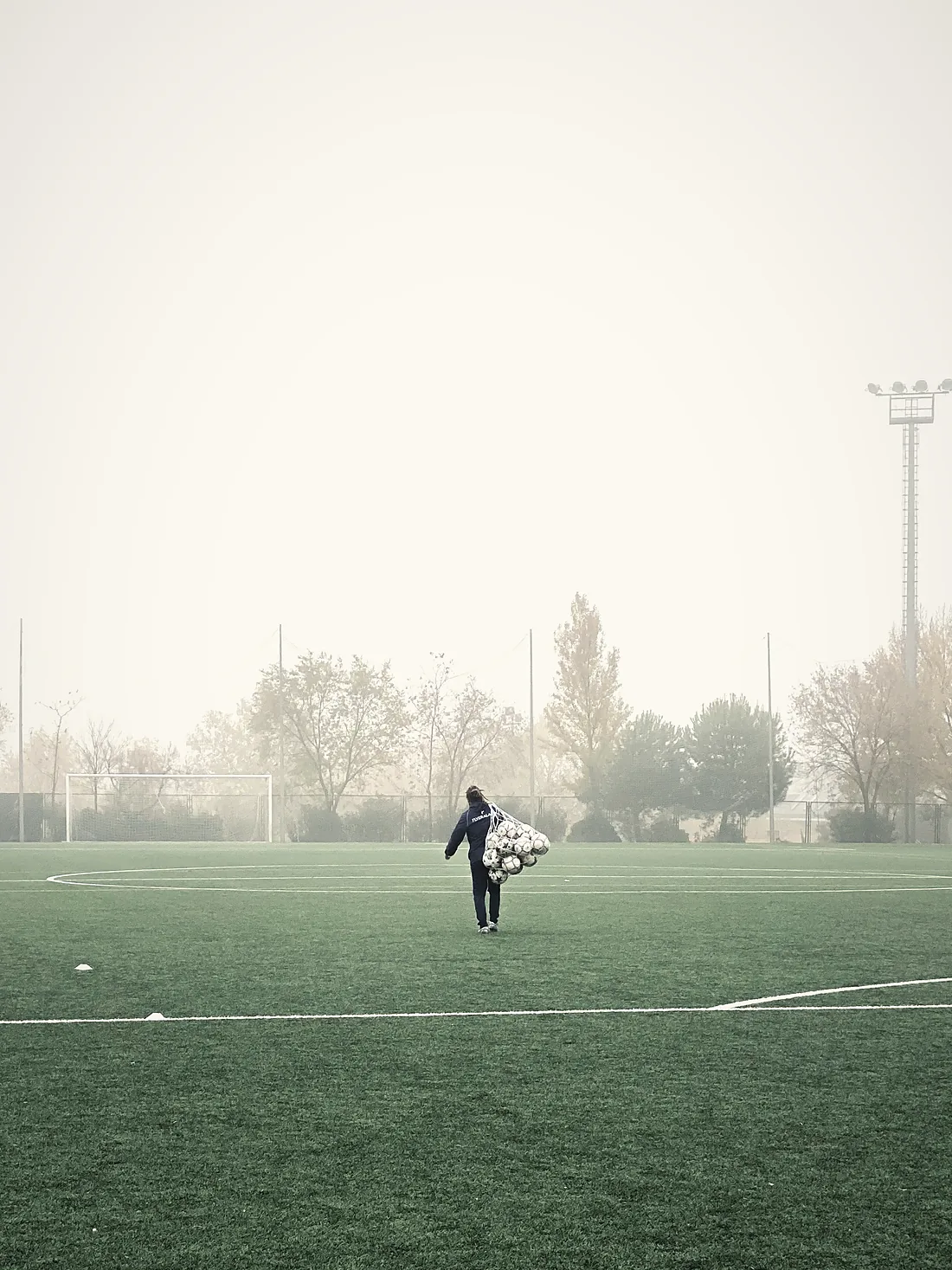 Cancha con niebla; una persona cruza cargando los balones del entrenamiento